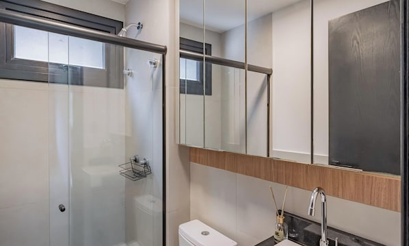 Ein modernes Badezimmer mit Duschkabine aus Glas, einer weißen Toilette und einem Waschbecken mit Spiegel darüber.