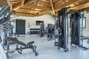 Ein Fitnessstudio mit unterschiedlichen Trainingsgeräten, einer Hantelbank und einem an der Wand montierten Fernseher.