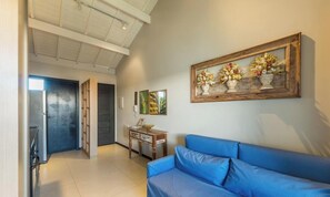 A living room with a blue sofa, a wooden coffee table, and a wall-mounted floral painting. - Apt in Condo w/ Pool in Praia do Forte Vlp0211 (Mata de São João)