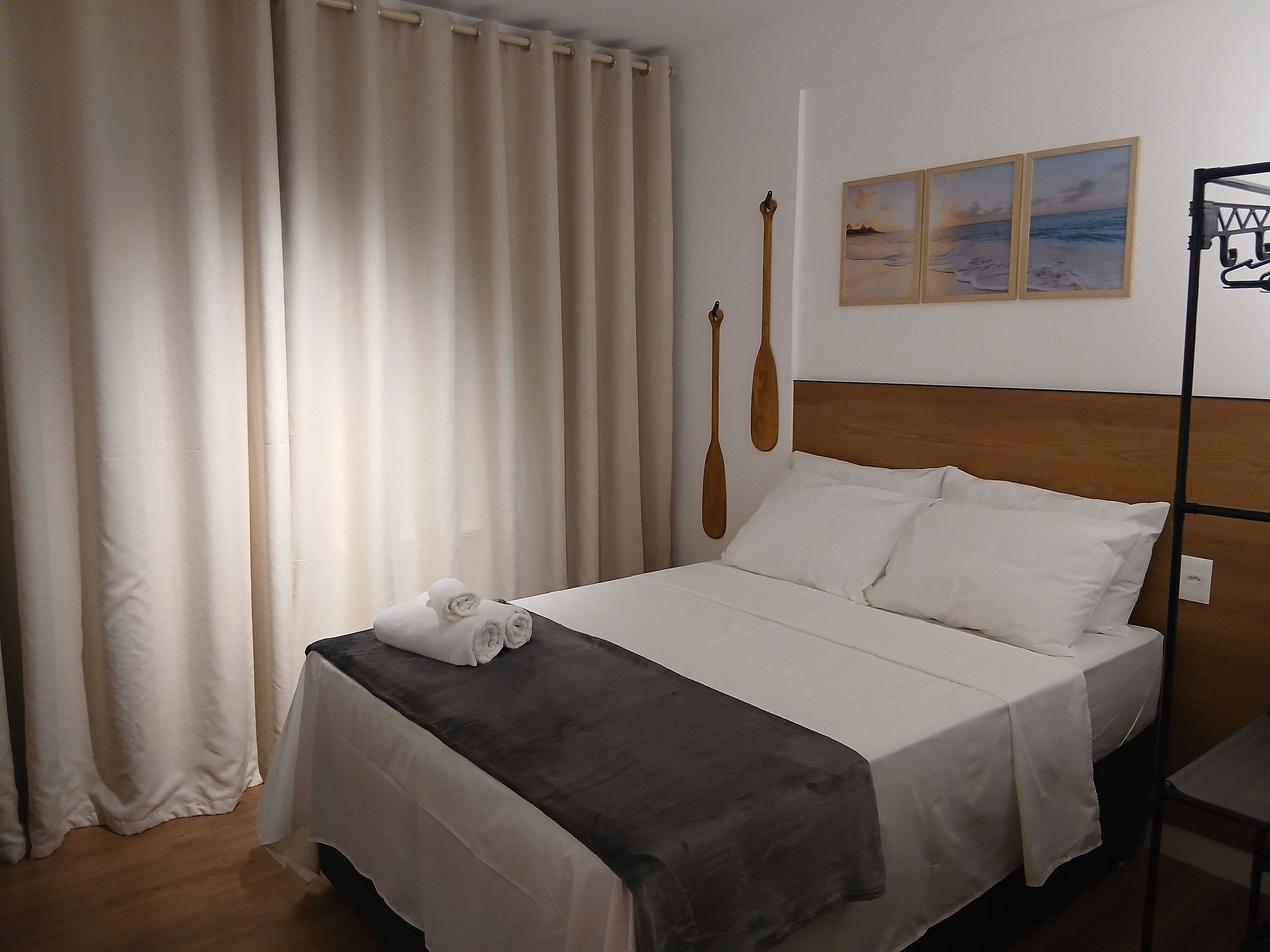 Een net opgemaakt bed met witte lakens en een donkere plaid, een houten hoofdbord, en een paar houten schepnetten aan de muur.