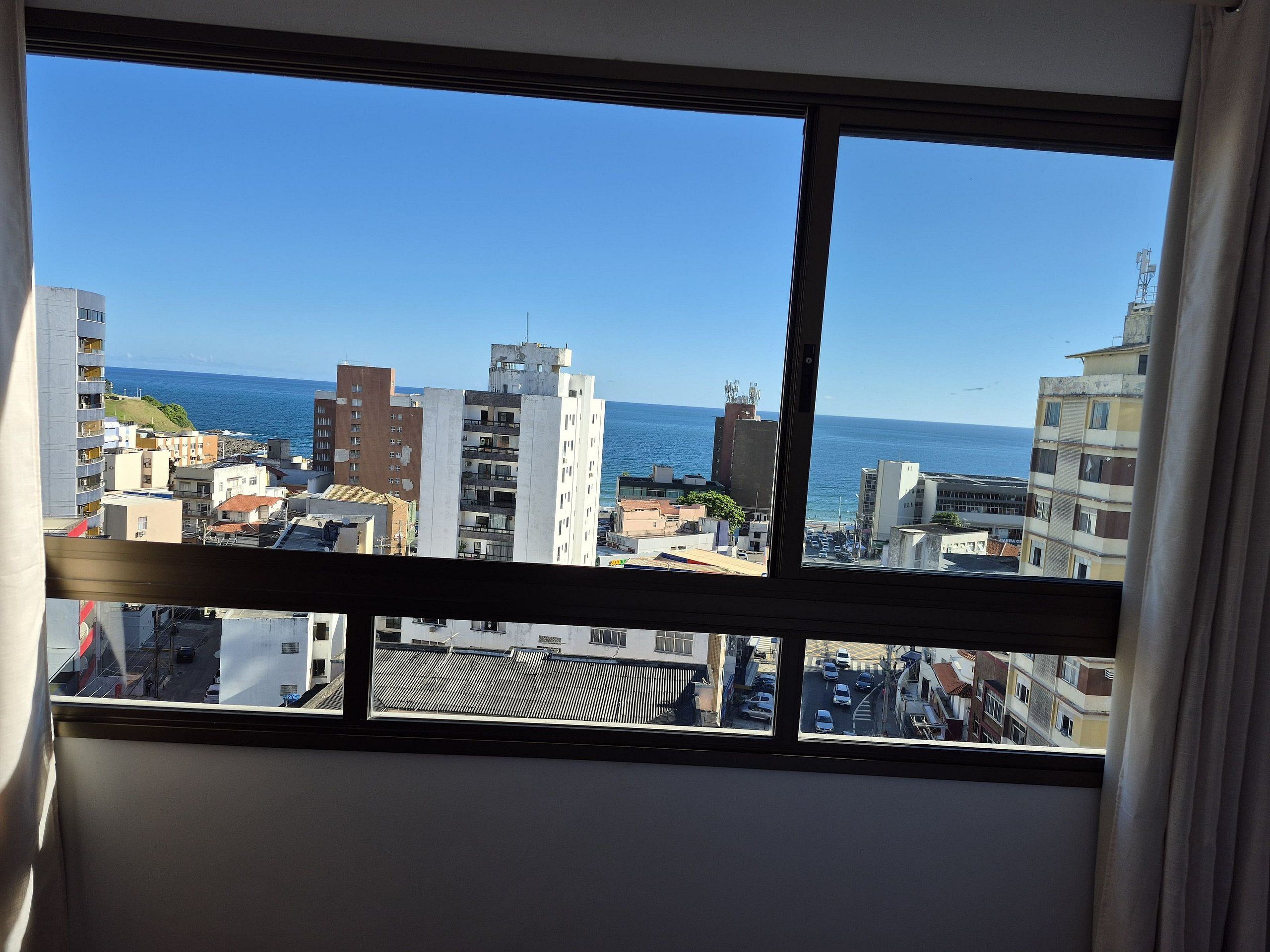 Une vue depuis une fenêtre donnant sur un paysage urbain, avec des bâtiments et un ciel bleu dégagé.