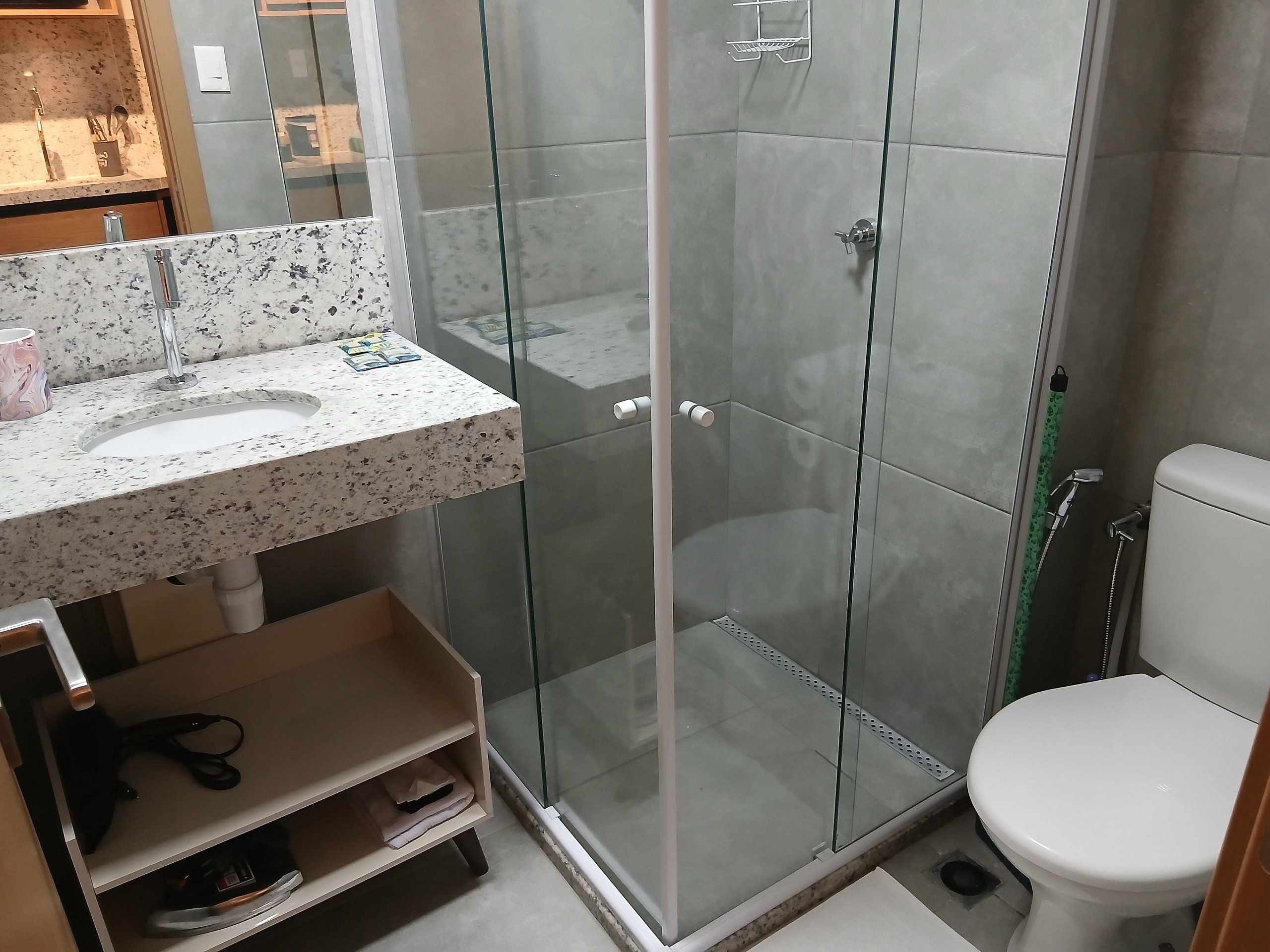 A modern bathroom with a glass-enclosed shower, a white sink with a speckled countertop, and a toilet.