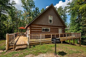 A cabin with a wooden deck, a grill, and a covered seating area. - Romantic, Secluded Log Cabin | 2BR, 1.5BA (Columbus)