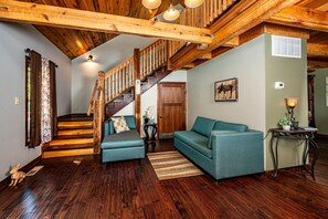 A wooden staircase with a wooden ceiling, a sofa, a small table with a lamp, and a wall-mounted picture. - Romantic, Secluded Log Cabin | 2BR, 1.5BA (Columbus)