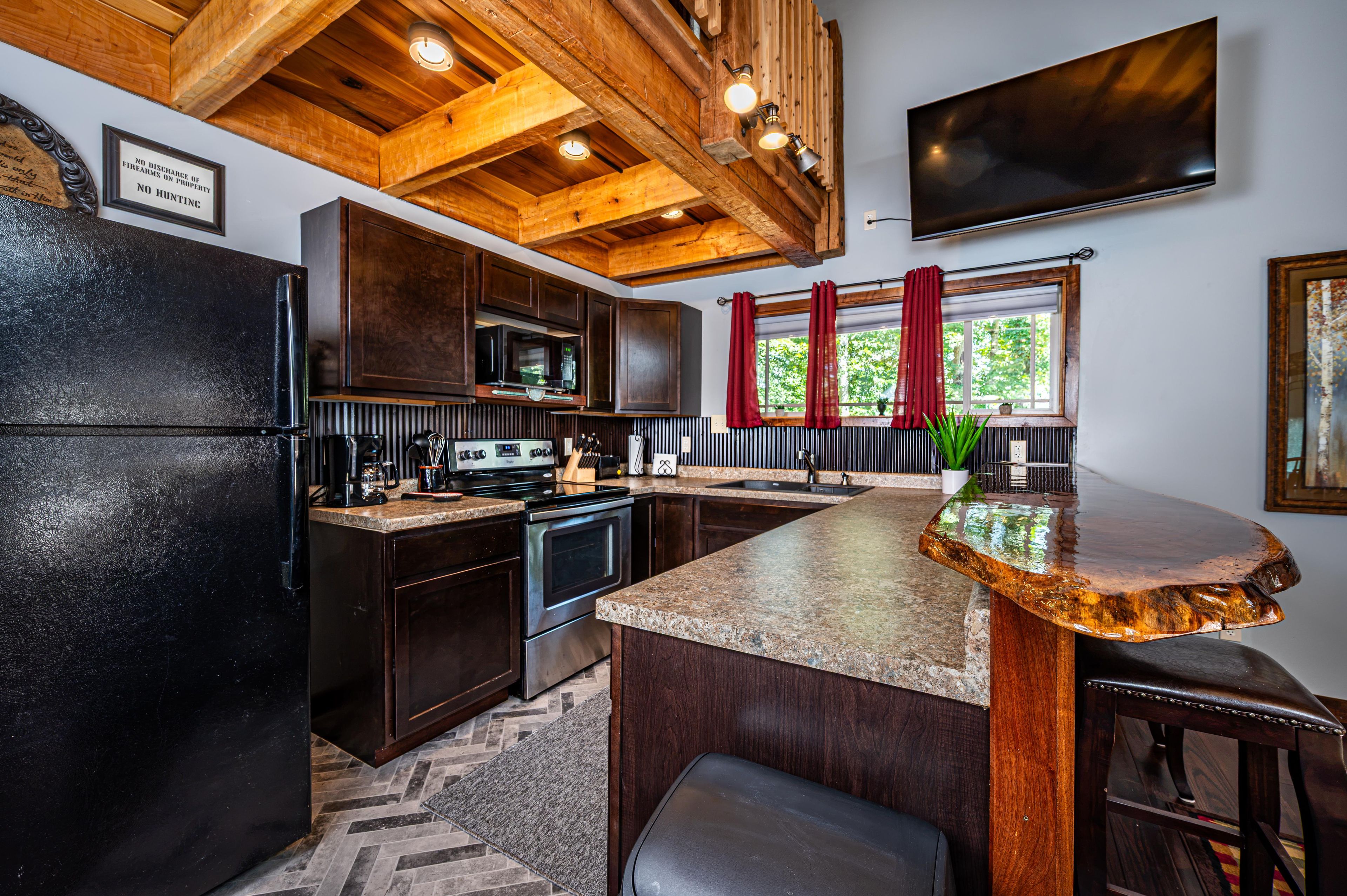 A kitchen with dark wood cabinets, a stainless steel refrigerator, a microwave, and a large island with a granite countertop.