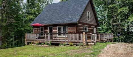 A log cabin with a porch and a red umbrella, surrounded by trees.