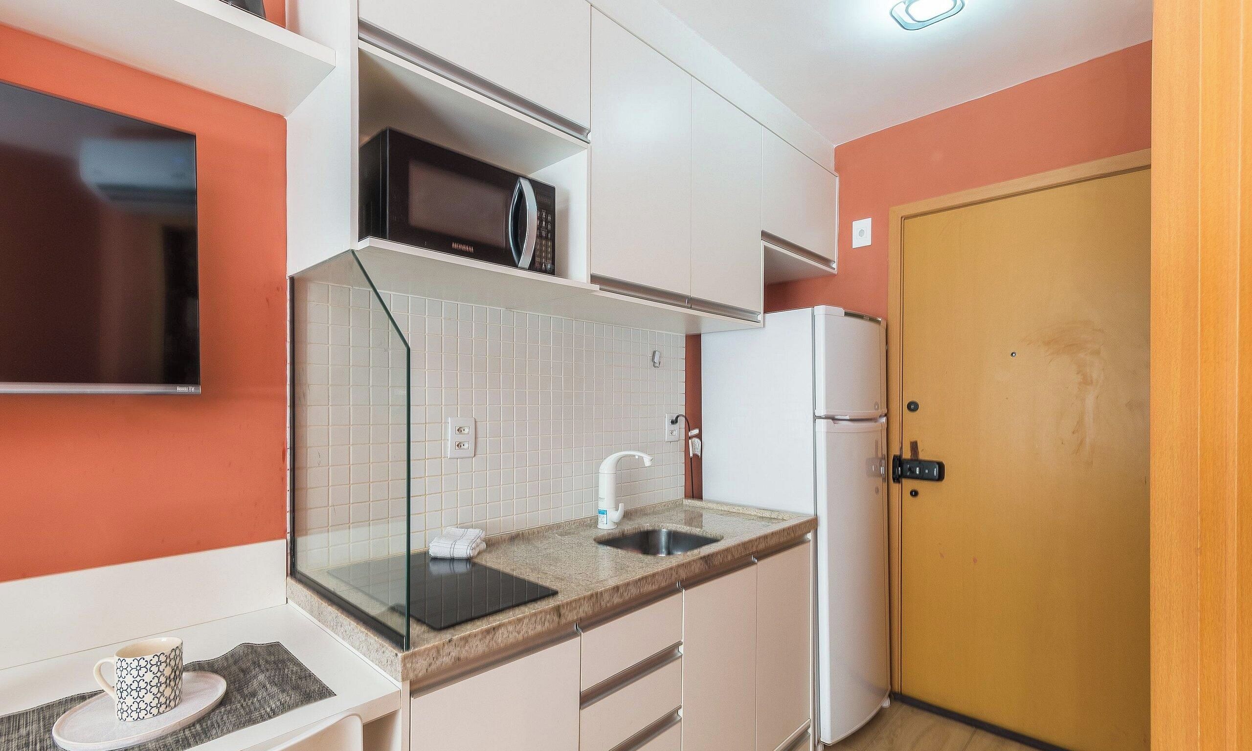 Cocina compacta con microondas, pileta y una puerta a la derecha.