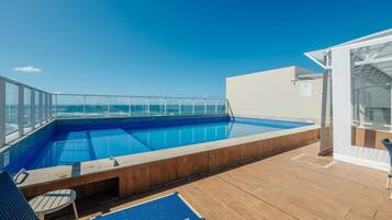 Une piscine sur le toit, avec une eau d’un bleu limpide, une balustrade en verre et une terrasse en bois.