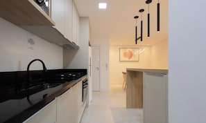 A modern kitchen with a black countertop, white cabinets, and a stainless steel range hood. - Apt w/ Barbecue, 500m From the Beach Stw1506 (Itapema)