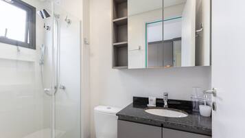 Ein modernes Badezimmer mit Duschkabine aus Glas, Toilette, Waschbecken mit Granitplatte und Spiegel mit Ablagefläche darüber.
