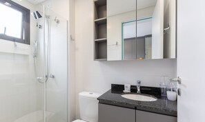 Ein modernes Badezimmer mit Duschkabine aus Glas, Toilette, Waschbecken mit Granitplatte und Spiegel mit Ablagefläche darüber.