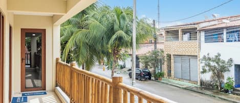 A balcony with a wooden railing overlooking a street with palm trees and parked cars.