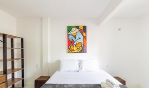 A hotel room with a bed, a bookshelf, and a colorful painting on the wall. - Modern Apartment, 160 m From Cumbuco Beach Mcu0103 (Caucaia)
