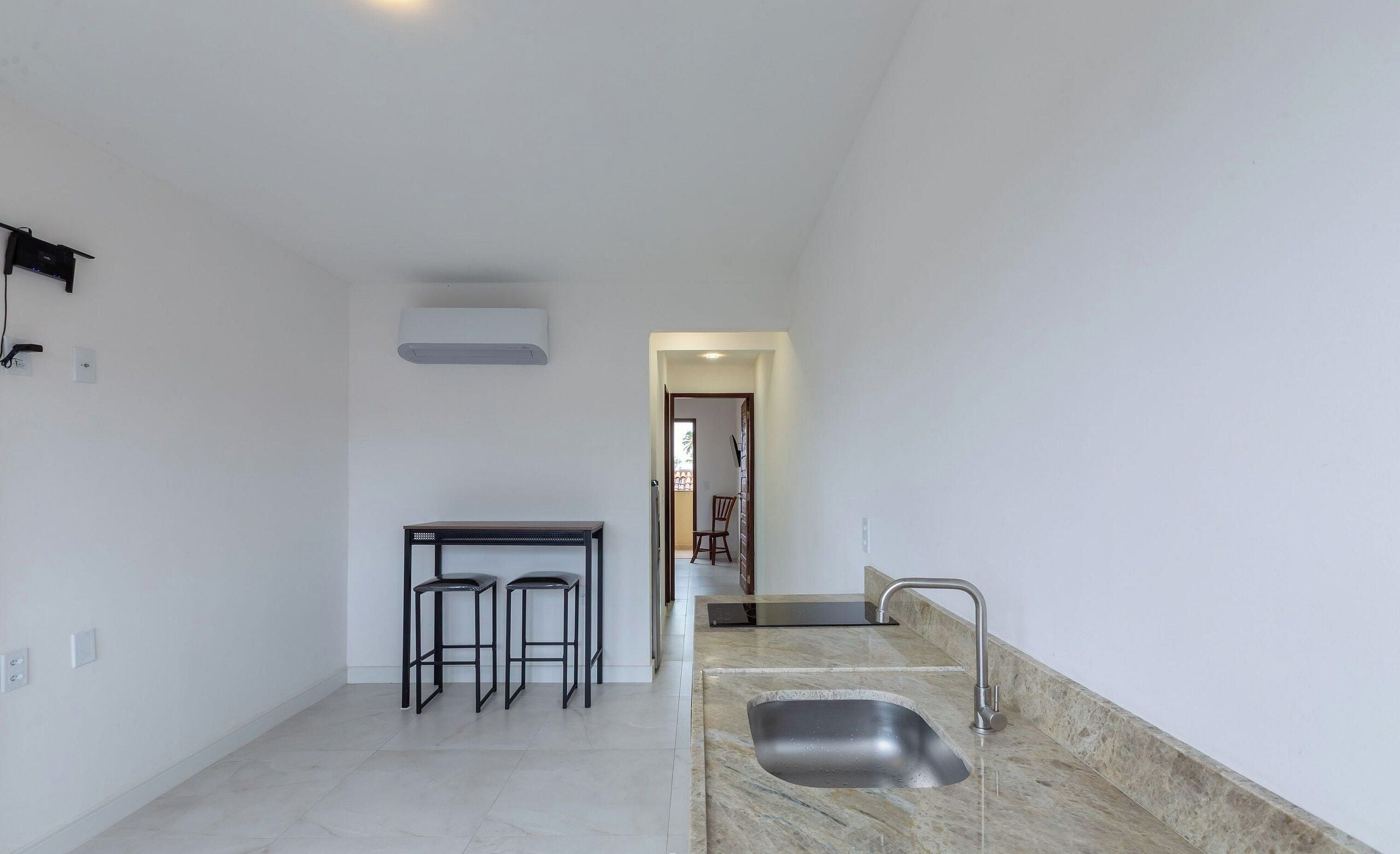 Una cocina moderna con un lavaplatos integrado, una zona de comedor con mesa y taburetes, y un pasillo que lleva a otra habitación.