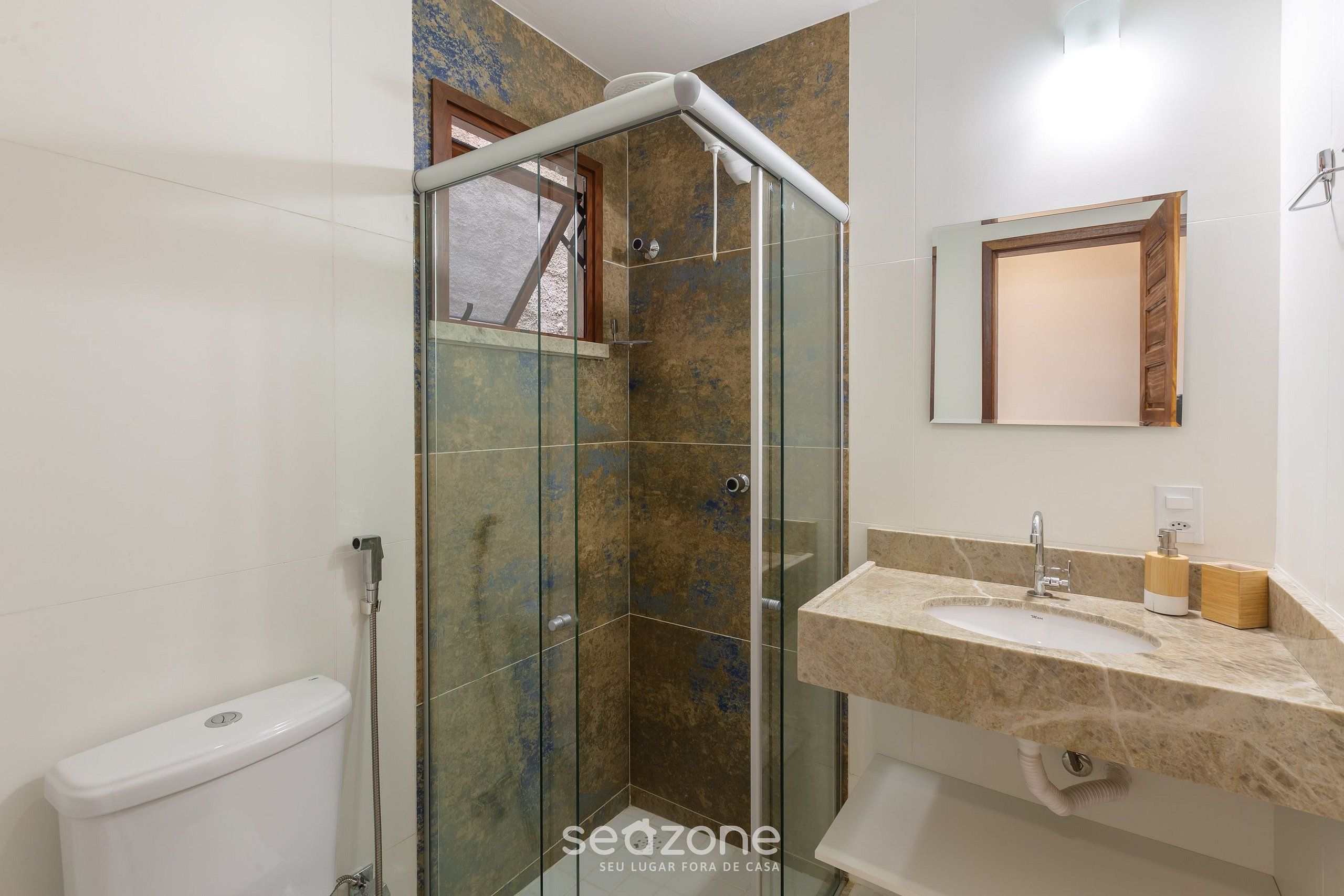 A bathroom with a glass shower enclosure, a toilet, a sink with a marble countertop, and a mirror.