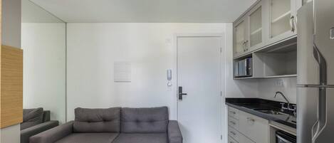 A compact living space with a kitchenette, a grey sofa, and a door leading to another room.