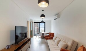 A modern living room with a flat-screen TV, a sofa, and a dining area with chairs. - Apartment w/ BBQ and sea View Arf1803 (Porto Belo)