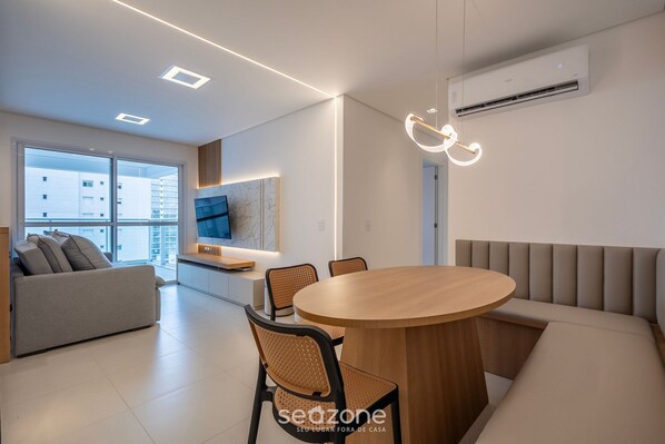 A modern living room with a sofa, a round wooden dining table, and a built-in bench.