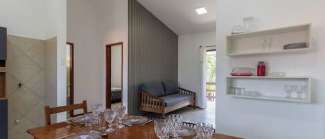 Un comedor con una mesa de madera preparada para una comida, un sofá y vistas al exterior.