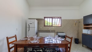 A dining area with a table set for four, a refrigerator, a stove, and a window with a view of greenery. - Apt in Condo w/ Pool 500m From the Beach Enl0002 (Porto Seguro)