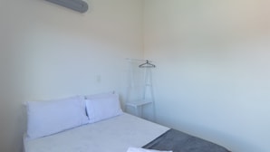 A simple, clean room with a bed, a white wall, and a small white shelf with a hanger. - Apt in Condo w/ Pool 500m From the Beach Enl0002 (Porto Seguro)
