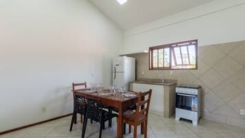 A dining area with a wooden table and chairs, a white refrigerator, a gas stove, and a window with a view of greenery.