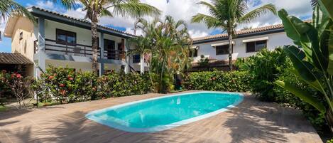 A swimming pool surrounded by lush greenery and a multi-story building with balconies.