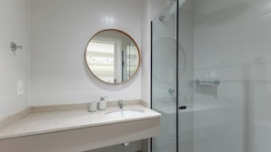 Casa de banho moderna com cabine de duche de vidro, espelho redondo e lavatório branco com bancada.