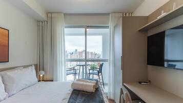 A hotel room with a bed, a desk, a chair, a TV, and a balcony with a city view.