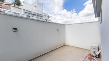 Un balcone pulito e vuoto con un muro bianco, una piccola pianta in vaso e un dispenser d'acqua.