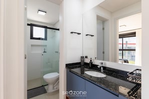 A modern bathroom with a glass shower enclosure, a white toilet, a black countertop, and a large mirror. - 1BR apt w/ BBQ in Curitiba Pla0201 (Curitiba)