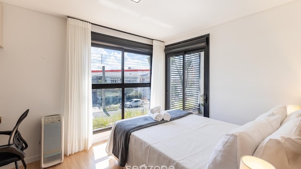 Ein Schlafzimmer mit einem Bett, einem Sessel, einem Heizgerät und einem Fenster mit Blick ins Freie.