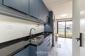 A modern kitchen with dark cabinets, a black countertop, stainless steel sink, and a microwave. - 1BR apt w/ BBQ in Curitiba Pla0201 (Curitiba)