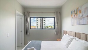 Ett hotellrum med en säng, ett fönster med gardiner, en tavla på väggen och en dörr.