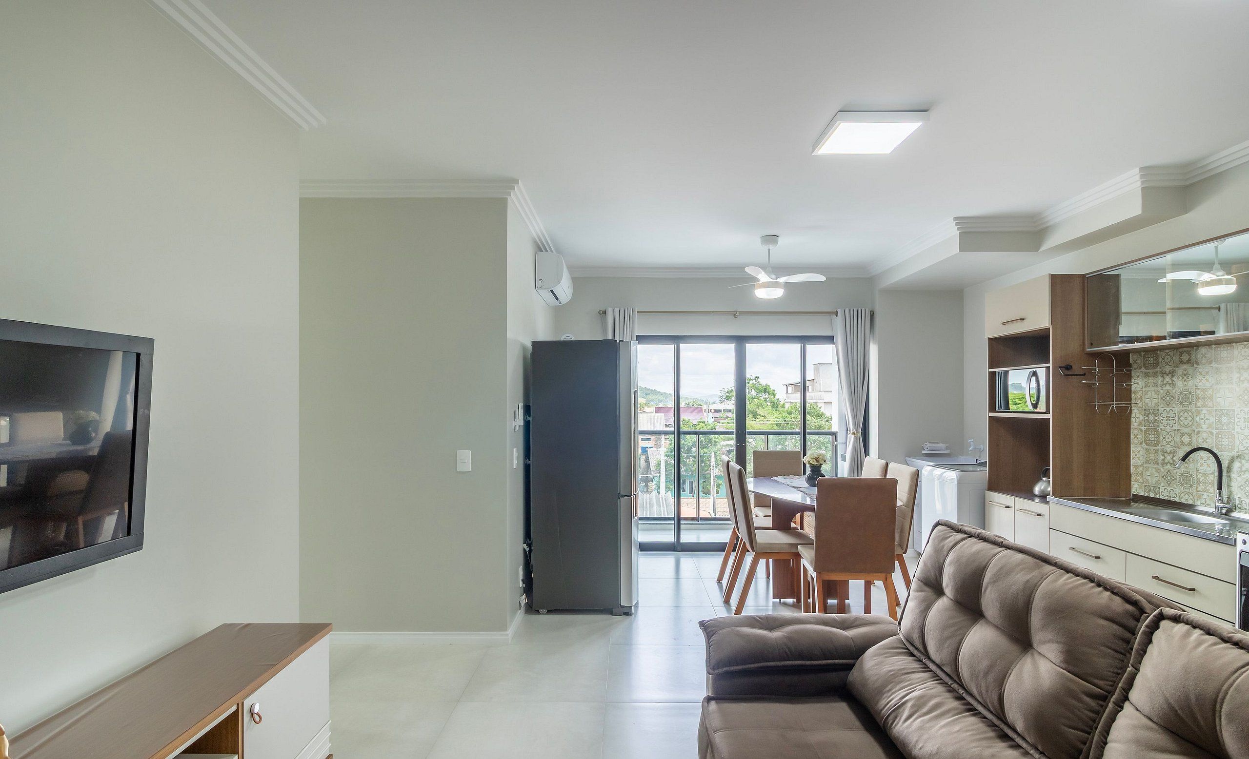 Una sala moderna con un sofá, un televisor, un comedor con sillas y una cocina con un fregadero y armarios.
