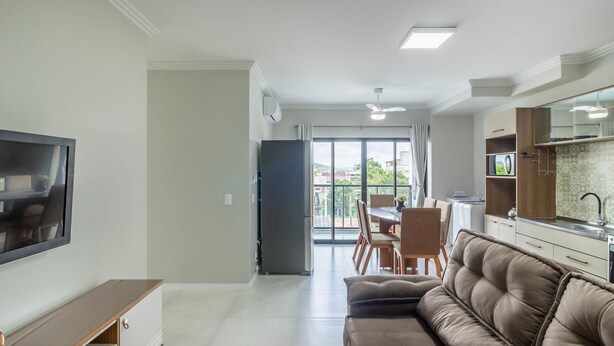 A modern living room with a sofa, a TV, a dining area with chairs, and a kitchen with a sink and cabinets. - Apt in Cond. w Pool, 650m fr/ Beto Carrero Lav0308 (Penha)