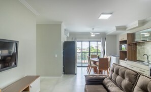Una sala moderna con un sofá, un televisor, un comedor con sillas y una cocina con un fregadero y armarios.