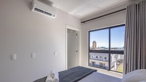 A hotel room with a bed, a window with a view of buildings, an air conditioner, and a door. - Apt 650m fr/ Beto Carrero in Cond w/ Pool Lav0401 (Penha)