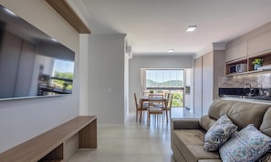 A modern living room with a flat-screen TV, a sofa with patterned cushions, and a dining area with a table and chairs. - Apt 650m fr/ Beto Carrero in Cond w/ Pool Lav0401 (Penha)
