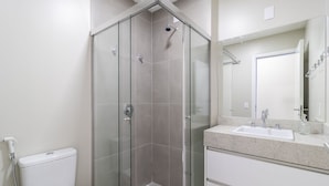 Ett modernt badrum med en dusch som är avskärmad med glasväggar, en vit toalett och ett handfat med en spegel ovanför.