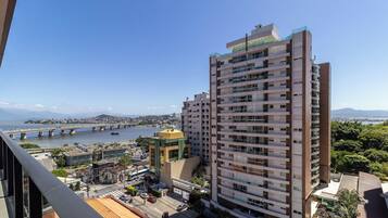 A high-rise building with multiple balconies, a view of a bridge, and a body of water in the background.