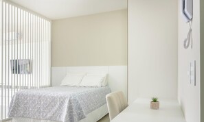 Quarto com cama, uma mesinha com uma planta e telefone fixado na parede.