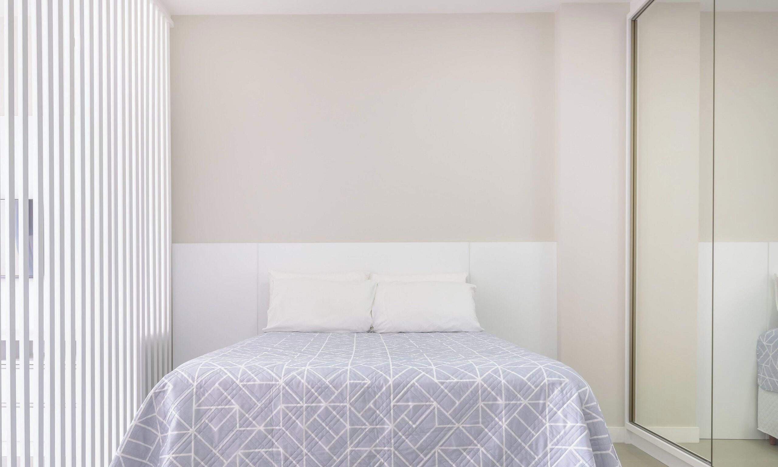 A bedroom with a bed, white headboard, and a large mirror.