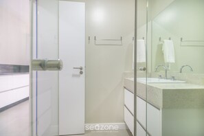 Uma casa de banho moderna com cabine de duche em vidro, porta branca e um espelho grande sobre a sanita.