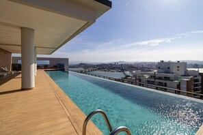 A rooftop infinity pool with clear water, wooden deck, and a view of the cityscape and mountains in the background. - Studio With sea View in Downtown Floripa Tvt904 (Florianópolis)