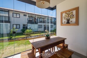 A room with a wooden table, a framed artwork of a tree, and a view of a building through large windows. - 2 Bedroom Apart in Condominium With Pool Vlp0111 (Mata de São João)