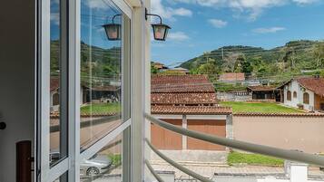 A balcony with a view of a residential area, including houses with tiled roofs and a car parked on the street.