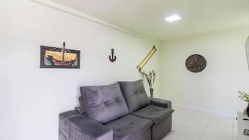 Ein Wohnzimmer mit grauem Sofa, einem gerahmten Gemälde, einer Wandhalterung, zwei Holzstöcken und einer runden Dekotasse.