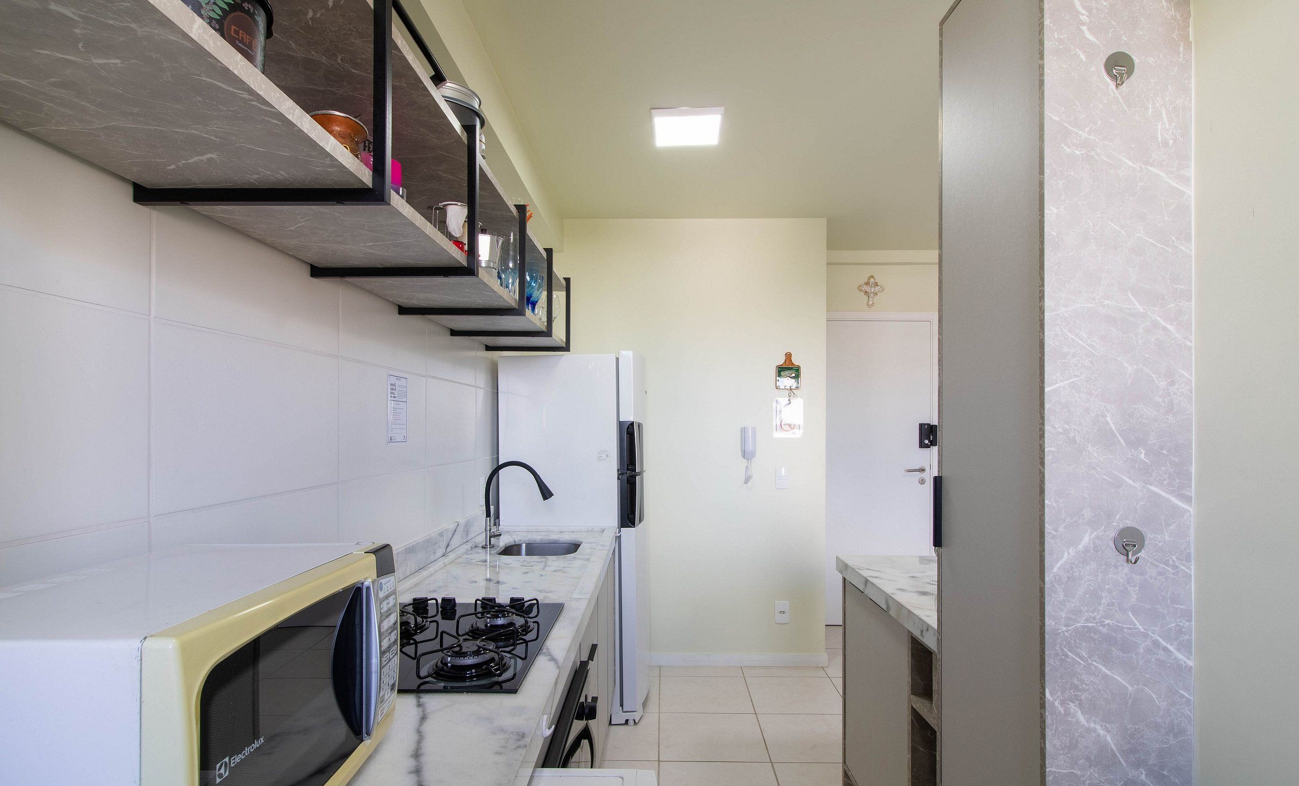 Eine moderne Küche mit Einbau-Mikrowelle, Herd und Spüle. Oberhalb der Spüle befindet sich ein Regal mit verschiedenen Gegenständen.