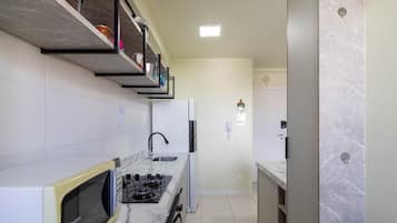 Eine moderne Küche mit Einbau-Mikrowelle, Herd und Spüle. Oberhalb der Spüle befindet sich ein Regal mit verschiedenen Gegenständen.
